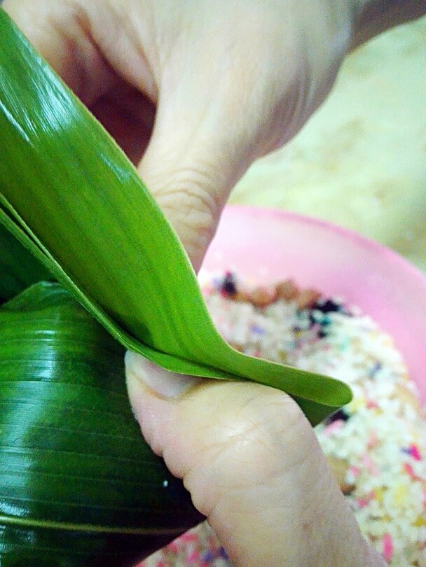 彩米花生香菇肉粽,包法主要在这步，左手手指往里压挤，右手也粽叶折上。