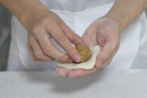 手工冰皮月饼,将加好果蔬粉的冰皮放掌心压扁。把绿豆馅放入冰皮上