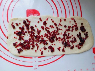 蔓越莓面包,取一块面团，用擀面杖擀长方形，然后再把切好的蔓越莓撒在擀好长方形面团上，(可以涂一层融化的黄油后再撒上蔓越莓)