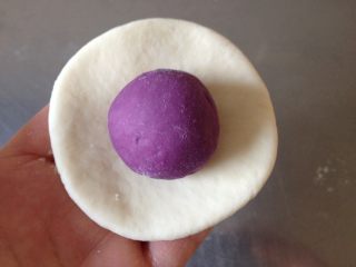 紫薯開花饅頭,取一個白面團搟成圓形面皮，再把紫薯球放在中間