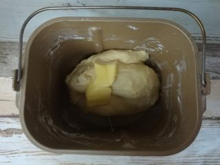 一次发酵软吐司,取出面团放入面包机，加入黄油，再次启动和面程序15分钟。