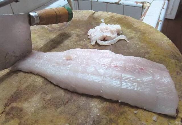 清汤鱼圆,2、取出鱼肉，鱼皮朝下放到砧板上，钉住鱼尾。