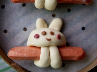香肠兔子馒头,取出之前发酵好的可可粉面团和红曲粉面团，做成兔子的眼睛嘴巴和腮红