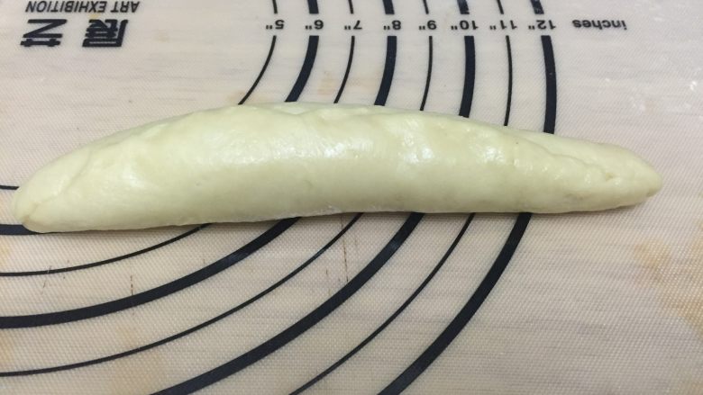 心形玉米火腿沙拉包,由上至下卷起，收紧收口，呈橄榄长形的面团。用刀横着切开面团，呈V字型