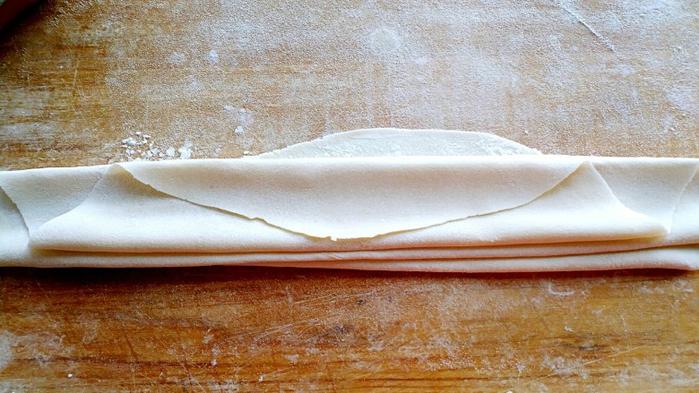 鲜虾鸡蛋手擀面,当擀压到两张饺子皮的厚度时，提起卷好面片的擀面杖，前后晃动，来回对折，每折一层撒干面粉防止粘连，如图，不宜过宽