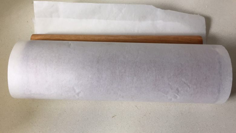 可可旋风瑞士卷（后蛋法）,擀面杖卷起油纸，起头轻压一下，就是刚刚划一条痕迹的地方，顺势卷起油纸，放置一边静止定型。
