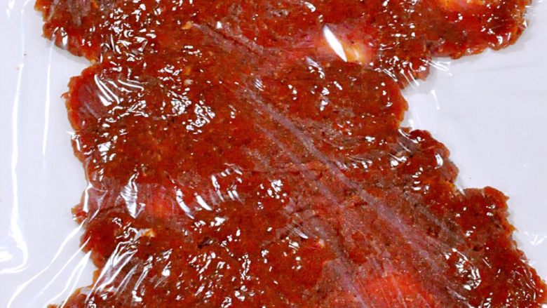 蜜汁黑椒肉脯,半小时后取出肉末，取1/4平铺在裁好的油纸上，肉末上面盖上保鲜膜。