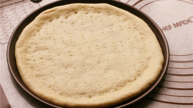 培根玉米粒披萨,放到披萨盘里，用叉子在面饼上扎出小孔。