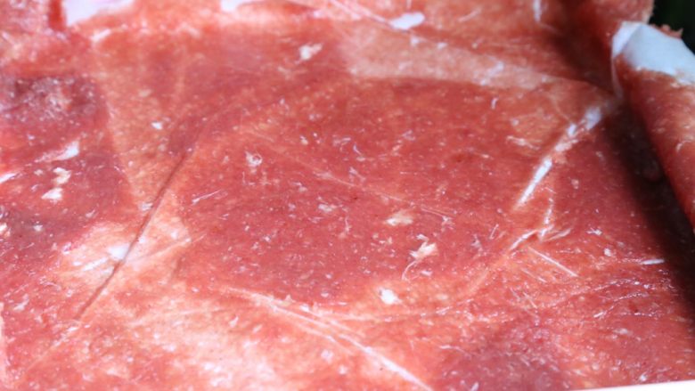 自制蜜汁猪肉脯,擀好后，揭去盖着的保鲜膜；被擀平的肉泥几乎可以透过油纸的厚度。