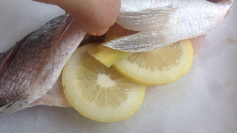 柠檬烤鱼,将鲈鱼放在已经铺了锡纸和油纸的烤盘上，两片柠檬和姜片放入到已经腌好的鱼肚里