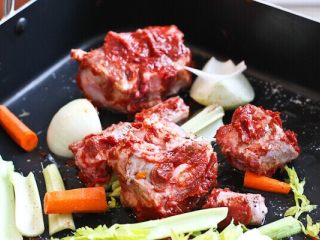 红酒牛肋排，一道完美的节日主菜,用番茄酱擦牛尾，放在烤盘中。添加洋葱，芹菜，胡萝卜和大蒜，只用1汤匙的烹饪油。