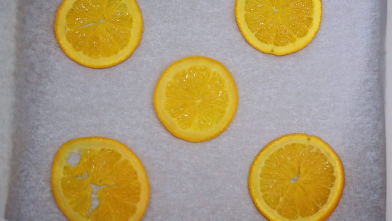 香橙蛋糕卷（清爽过夏天）,把煮好的橙片捞出，用厨房纸吸干，然后放在铺好烤纸的烤盘里，如图摆好备用。
另外，糖水放凉。