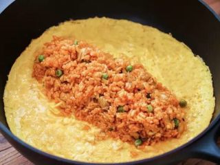 治愈系蛋包饭,关火，米饭放在蛋皮中间，翻起蛋皮的一边将米饭包住，把锅倾斜后翻扣在盘中