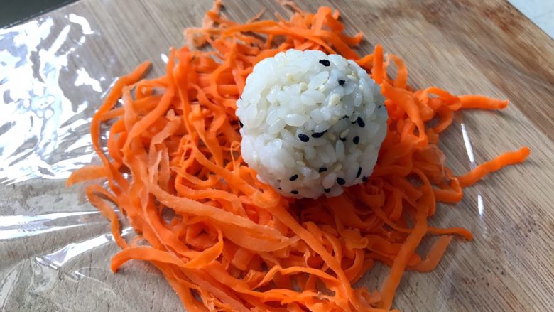 日式手鞠壽司飯團,胡蘿蔔鋪在保鮮膜上，手沾一點點水捏一個大小合適的小飯團放在胡蘿卜上面。