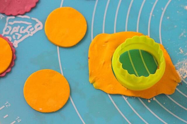 ［鹿小鹿］翻糖卡通纸杯蛋糕,取小号的圆形饼干模，在黄色的翻糖片上切出圆形，用清水粘贴在淡紫色的翻糖片上。