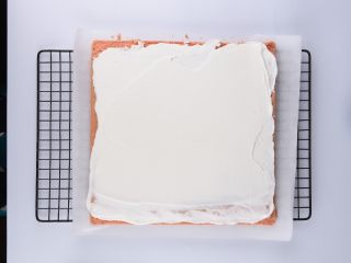 草莓花式蛋糕卷,将打发的蛋奶油抹在蛋糕胚表面，中间抹厚点，两边薄一点奶油