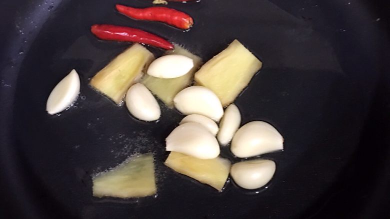 红烧青占鱼,热火以后，倒入油，烧至7成热的时候放入蒜、姜和辣椒，翻炒半分钟。