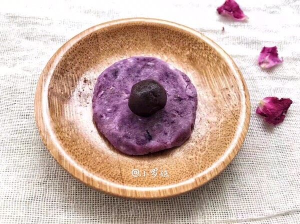 紫薯椰蓉球,把紫薯团压手压扁，豆沙团放上面，紫薯面团由外向内慢慢收口，把豆沙包裹住，慢慢搓成圆球。

