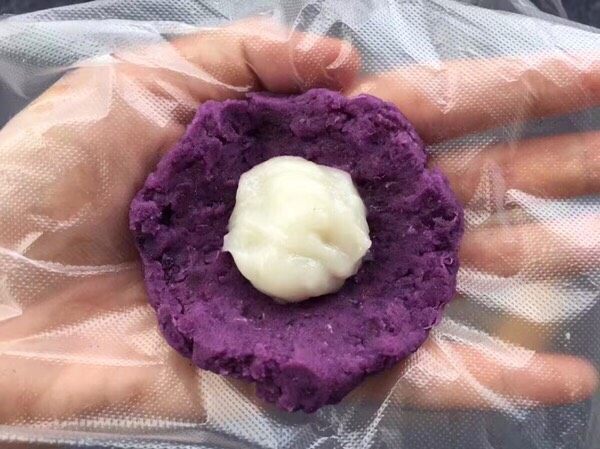 紫薯茶巾布绞,再取一勺糯米泥放入，紫薯泥慢慢由外向内收口，把糯米团包裹着。



