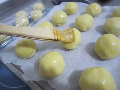 咬一口酥软掉渣的蛋黄酥,稍加整理成型收口朝下放在铺了油纸的烤盘里。表面刷蛋黄液
