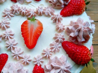 水果奶油生日蛋糕,边缘用大裱花嘴挤出花，奶油草莓一分为二。一朵花，一颗草莓的摆一圈。中间用小裱花嘴挤出自己想要的图案