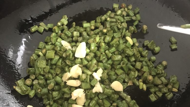 干煸橄榄肉沫豆角,炒5分钟左右，待到豆角表皮慢慢变皱，下入蒜，慢慢翻炒