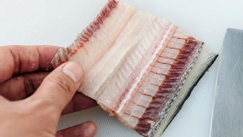 香煎无刺带鱼,带鱼块平放在菜板上，紧贴这鱼鳍位置把带鱼骨刺片下来。