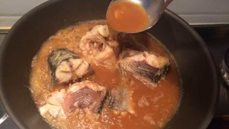 家常炖鱼,用勺子往未淹没在汤中的肉上浇汤汁