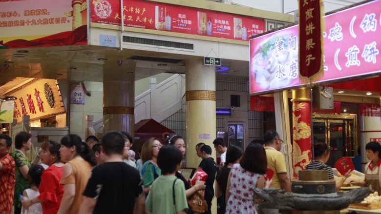 天津老味煎饼果子,天津南市食品街的煎饼果子摊一共有四个摊位，东西南北门各有一个摊位，这是游客们买煎饼果子排队的情景。