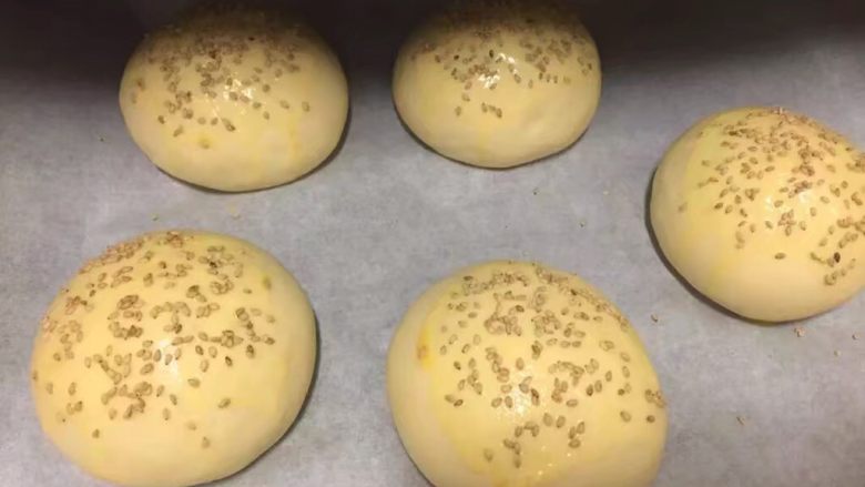 自制麦辣鸡腿汉堡,取出后，面包胚表面刷一层蛋黄液，上面撒上适量白芝麻