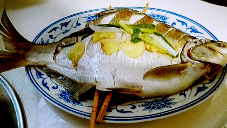 好想吃~清蒸鳊鱼,再用夹子取出鱼盘，倒掉盘子里面的蒸鱼的水，抽掉筷子，去掉鱼上面的葱姜