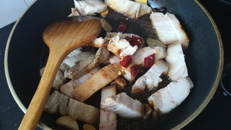 家常红烧肉,糖开始起泡后立即倒入切好的肉和香叶、辣椒快速翻炒