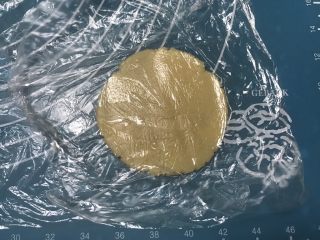 广式五仁月饼,取一个面团放在保鲜膜上用手掌摁一下 ，然后上面盖上保鲜膜擀成圆形，