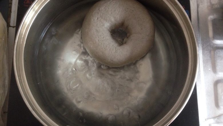 黑芝麻贝果,将50克糖放进装了1千克水的锅里，煮开，提起油纸将贝果放入到锅里，两面各煮20秒，用筛网将贝果捞起，沥干水分，放在不粘烤盘上