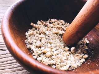 小森林系·温暖醇香的糙米核桃饭,把核桃仁放在一个深一些的碗里，用木棒捣碎。捣的时间不要太用力，核桃仁会蹦出来。

不用捣成泥，留一些颗粒吃起来会更香。
核桃碎做好后，放在一旁备用。