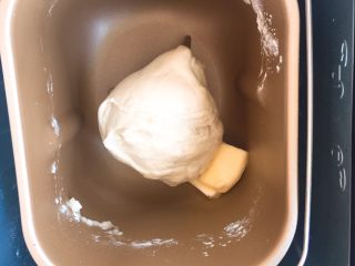 超级松软的    炼乳小面包,揉至光滑的面团后，放入黄油，继续启动揉面程序，揉至出现手套膜的程度就可以了。