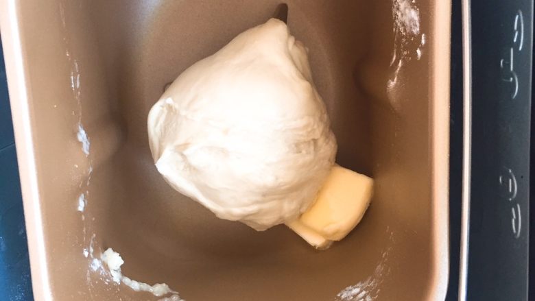 超级松软的    炼乳小面包,揉至光滑的面团后，放入黄油，继续启动揉面程序，揉至出现手套膜的程度就可以了。