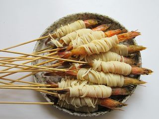 私家茄汁金丝虾串,将面条几根理顺在一起，缠绕在虾的中间身体部位
