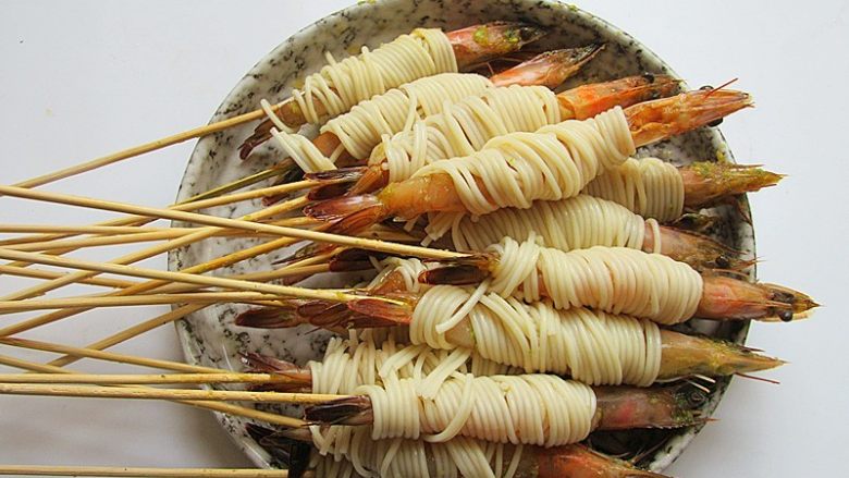 私家茄汁金丝虾串,将面条几根理顺在一起，缠绕在虾的中间身体部位
