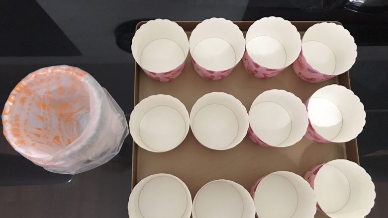 棒棒糖蛋糕,首先将纸杯在烤盘上摆好，裱花袋套在杯子上。因为棒棒糖蛋糕需要制作4种颜色的蛋糕糊，翻拌时间比普通戚风蛋糕时间长，所以提前做好准备以免蛋白霜消泡过度。