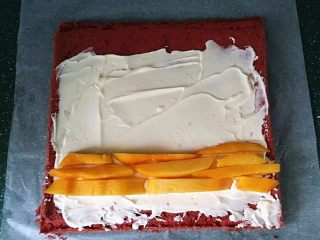 红丝绒蛋糕卷,将蛋糕的正面向上、抹上淡奶油、放入芒果条