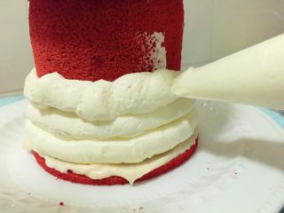 覆盆子红丝绒蛋糕,把香缇奶酪奶油装到裱花袋中将中间和顶部蛋糕卷部分涂满