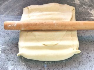 牛角可颂,然后用擀面杖按压的方式，将面团轻轻的擀成长方形，擀面过程当中要注意不让黄油露出来，大理石台面一定要铺一层薄面粉，在擀面过程当中随时检查底部是否粘在台面上。同样的道理，面团表面一样要铺一层薄面粉，不能让擀面杖把面皮粘下来，所以要随时搓掉擀面杖上面的面皮，如果有露出黄油的地方，一定要撒上干面粉再擀。