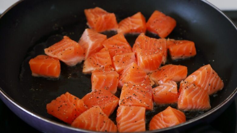 双椒土豆三文鱼,锅里多倒些油，油热将三文鱼块下锅，撒些黑胡椒碎和盐。