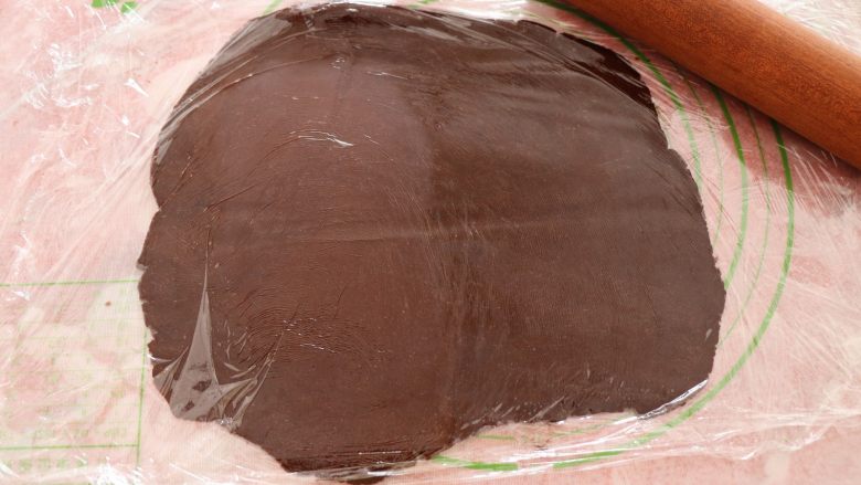 熊猫饼干,将可可色面团铺在硅胶垫上，上下各覆盖一层保鲜膜，用擀面杖擀成厚度大概3mm厚的面皮；