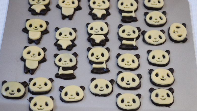 熊猫饼干,用同样的方式将原色面团擀成薄皮后用模具按压出脸部外形、表情部分、腹部部分，然后依次摆在可可面团的熊猫形状上；