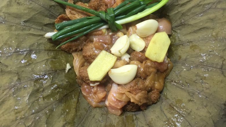 荷香蒸猴头菇鸡腿肉（附如何清洗猴头菇）,将荷叶铺开，放入腌制好的猴头菇鸡腿肉。表面摆上葱结，蒜子，姜。