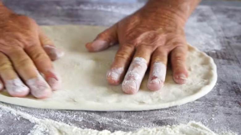 卡布里乔莎披萨,用手轻轻把面片展开，翻转一次，再加上一些面粉，接着如果你喜欢的话，可以用擀面杖把面团再擀开一些。
