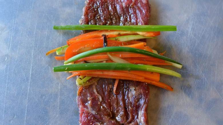 香煎牛排卷,把一条牛肉条摊平，在中间放上蔬菜丝和小葱，然后把牛肉卷起来。