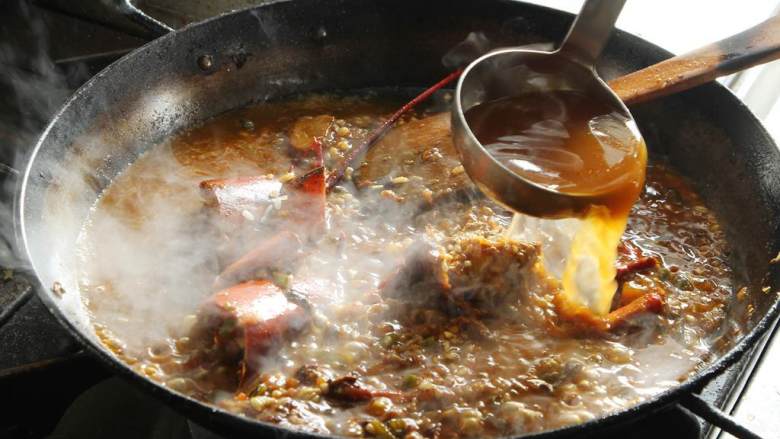 波士顿龙虾海鲜饭,加入龙虾高汤直至浸没所有食材，撒上适量盐和黑胡椒。高火先煮5分钟，以防米饭过快煮烂。